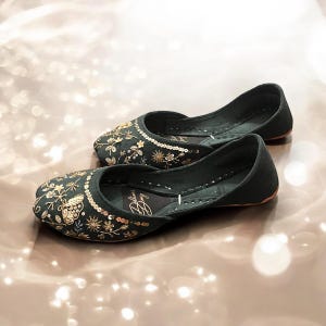 Pu&ograve; includere: Un paio di scarpe basse ricamate di colore verde scuro con filo dorato e paillettes. Le scarpe hanno un design floreale con farfalle.
