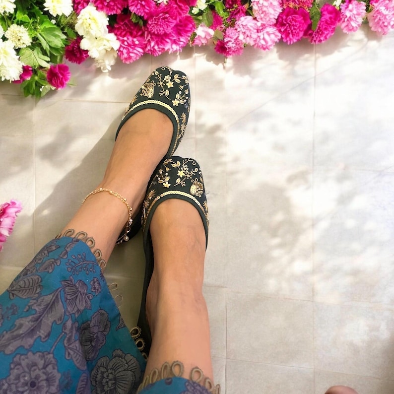Pu&ograve; includere: Un paio di scarpe basse verde scuro ricamate con dettagli in filo dorato. Le scarpe hanno una punta a punta e un tacco basso.