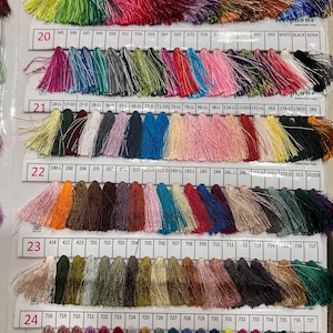 May include: A color chart of embroidery thread tassels in various colors, including green, red, pink, and blue. The chart is labeled with numbers and codes, and the brand name "NEELAM THREAD PVT. LTD." is visible.