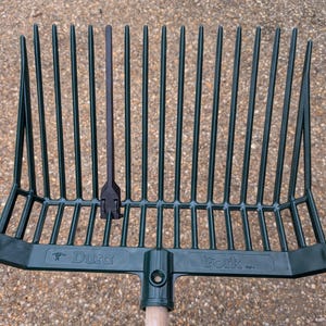 Könnte beinhalten: Grüne Plastik-Mistgabel mit einem Holzstiel. Die Gabel hat einen Metallansatz für den Stiel. Die Gabel ist mit "Dur-a-Fork" beschriftet.