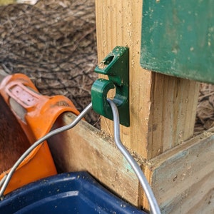 Könnte beinhalten: Ein grüner Plastikhaken, der an einem Holzpfosten befestigt ist, mit einem Metalldraht, der am Haken befestigt ist. Ein blauer Eimer hängt am Draht.