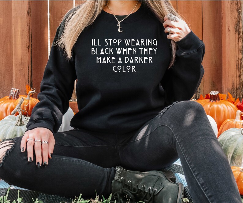 May include: A black sweatshirt with the text "I'll stop wearing black when they make a darker color" in white lettering.