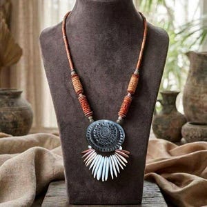 May include: A necklace featuring a large, dark gray circular pendant with an intricate embossed pattern, accented by a fringe of white and light brown tapered beads. The cord includes cylindrical brown beads with carved details.