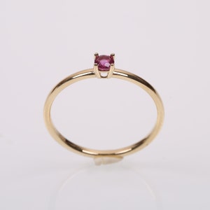 Puede incluir: Un delicado anillo de oro con una pequeña piedra preciosa redonda de color rosa engastada en garras.