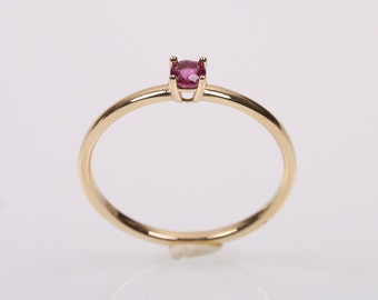 May include: A delicate gold ring with a small, round, pink gemstone set in a prong setting.