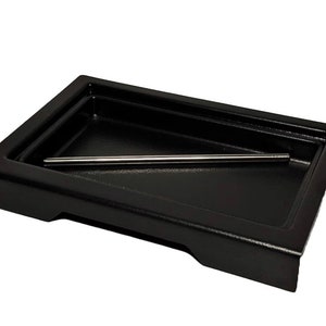 May include: A black rectangular tray with a raised edge and a metal rod inside. The tray is made of a durable material and is perfect for organizing small items.