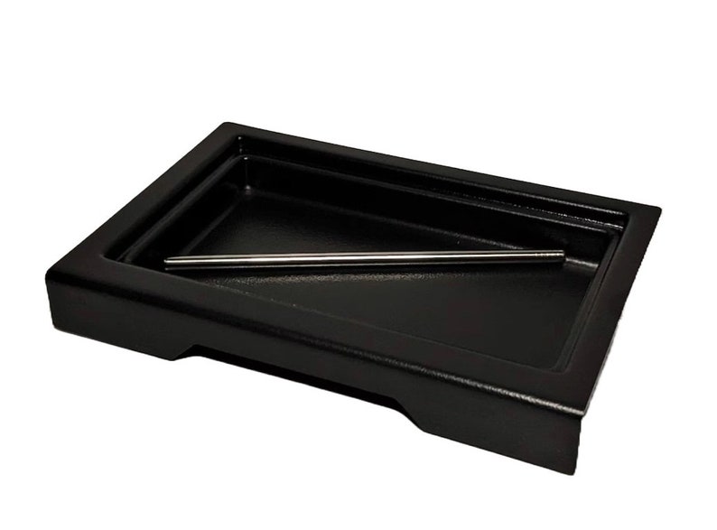 May include: A black rectangular tray with a raised edge and a metal rod inside. The tray is made of a durable material and is perfect for organizing small items.