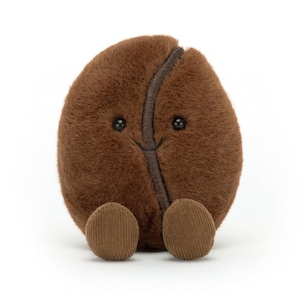 Puede incluir: Un juguete de peluche con forma de grano de caf&eacute; marr&oacute;n, con una cara sonriente y peque&ntilde;os pies de pana. El grano tiene una costura marr&oacute;n oscuro en el centro y peque&ntilde;os ojos negros de bot&oacute;n. El juguete es suave y tierno.