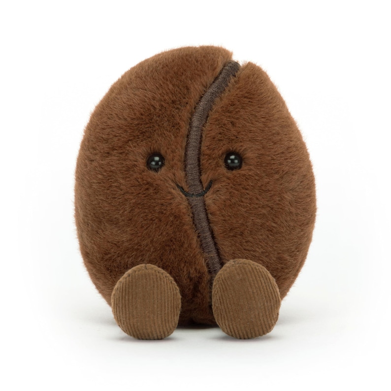 Puede incluir: Un juguete de peluche con forma de grano de caf&eacute; marr&oacute;n, con una cara sonriente y peque&ntilde;os pies de pana. El grano tiene una costura marr&oacute;n oscuro en el centro y peque&ntilde;os ojos negros de bot&oacute;n. El juguete es suave y tierno.
