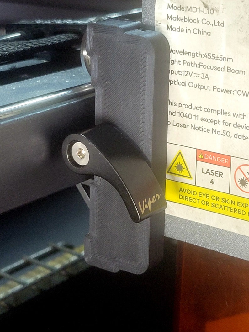 May include: A black plastic laser safety switch with the word "Viper" printed on it. The switch is attached to a laser engraver with a warning label that reads "DANGER LASER 4 AVOID EYE OR SKIN EXPOSURE TO DIRECT OR SCATTERED RADIATION".