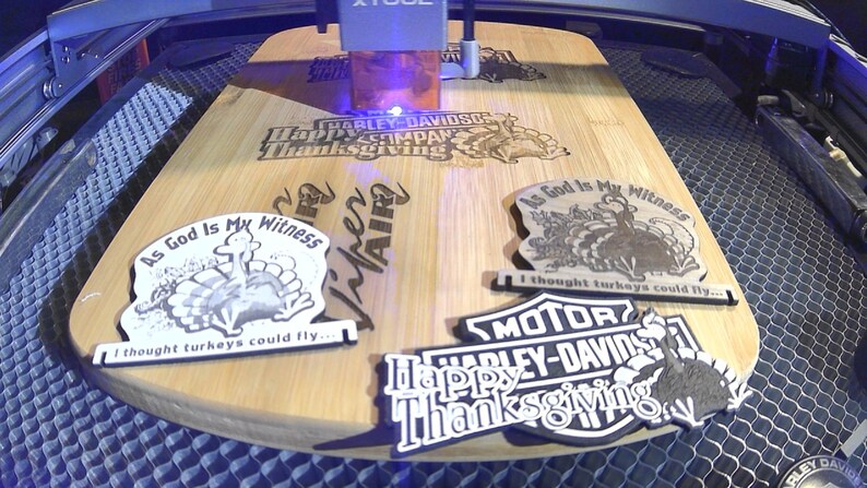 May include: A wooden cutting board with laser-etched designs, including Harley-Davidson logos and Thanksgiving-themed graphics. The board also features the text "As God Is My Witness" and "I thought turkeys could fly..."