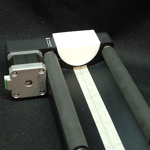 May include: A black and silver machine with two black rollers and a white plastic piece on top. The machine has a small motor with a green label that says "3".