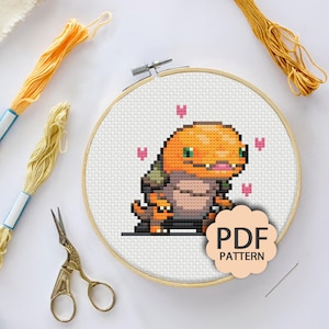 May include: Cross stitch pattern featuring a pixelated orange and brown creature with a small orange and brown creature on its back. The pattern is surrounded by pink hearts and the text "PDF PATTERN".