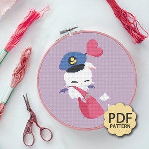 May include: A cross-stitch pattern featuring a white rabbit wearing a blue cap with a yellow emblem, a red scarf, and a red bag. The rabbit is holding a white envelope and has a red heart balloon attached to its ear. The pattern is displayed in a pink embroidery hoop on a white background.