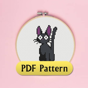 May include: A black and white cross stitch pattern of a black cat with purple ears, sitting on a white background. The pattern is in a round embroidery hoop. The text "PDF Pattern" is on a yellow banner below the hoop.