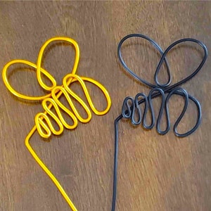 May include: Two wire bee sculptures, one gold and one black, on a wooden surface.