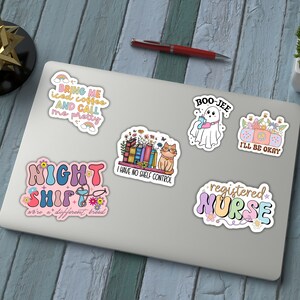 May include: A set of 7 colorful stickers with various designs and text. The stickers feature a ghost, a cat, a book stack, a stethoscope, a coffee cup, a flower, and a peace sign. The text on the stickers includes "Bring me iced coffee and call me pretty", "Night Shift", "I have no shelf control", "Boo-Jee", "I'll be okay", "registered nurse", and "we're a different breed".