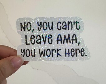 May include: A white glitter sticker with black text that reads "No, you can't Leave AMA, you work here." The sticker has a wavy outline and is held by a hand against a white marble surface.