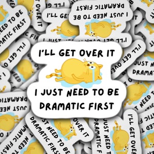 May include: A collection of white stickers with a cartoon cat illustration. The cat is yellow with a striped tail and is crying. Text on the stickers reads "I'll get over it" and "I just need to be dramatic first."