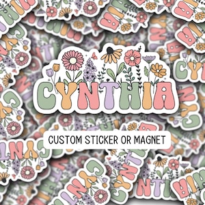 May include: A custom sticker or magnet with the name "CYNTHIA" in colorful, retro-style lettering. The name is surrounded by a border of flowers in shades of pink, purple, green, and yellow.