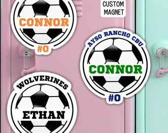 May include: Three soccer-themed locker magnets with black and white soccer balls, white outlines, and different team names and numbers. The top magnet says "FBCU CHRISTIAN CONNOR #0" in orange and black text. The middle magnet says "AYSO RANCHO CBU CONNOR #0" in blue, green, and black text. The bottom magnet says "WOLVERINES ETHAN #7" in black text.