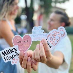 May include: Three stickers with a pink heart, a woman breastfeeding, and the text "Eat Sleep Breastfeed Repeat" in pink and blue. The stickers say "Milky Mama", "Eat local", and "Mama".
