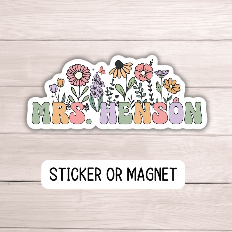 K&ouml;nnte beinhalten: Ein Aufkleber oder Magnet mit dem Namen "MRS. HENSON" in bunten, abgerundeten Buchstaben, umgeben von einem Blumendesign mit rosa, orangefarbenen, gelben und lila Blumen. Der Text "STICKER OR MAGNET" steht darunter.