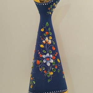 May include: A navy blue ceramic vase with a flared top and a gold rim. The vase is decorated with hand-painted flowers in white, red, yellow, and green. The vase is approximately 10 inches tall.