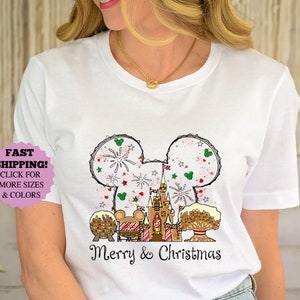 May include: A white short-sleeve t-shirt featuring a graphic of a mouse-ear silhouette filled with fireworks, a castle, and holiday treats. Below the graphic, the text Merry & Christmas is printed in a black script font on the front of the shirt.