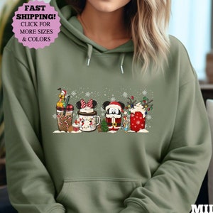 Peut inclure: Un sweat à capuche vert avec un motif de Noël représentant Mickey Mouse, Minnie Mouse, Pluto et Dingo. Le motif comprend une tasse, une chaussette et une tasse de chocolat chaud.