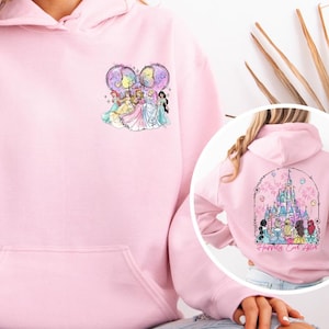 May include: A light pink hoodie with a front pocket and a drawstring hood. The front features a colorful graphic of cartoon princesses. The back of the hoodie has a castle graphic with the text "Happily Ever After".