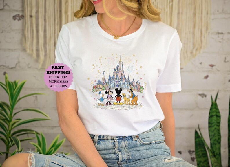 May include: White t-shirt featuring a colorful illustration of a castle and cartoon characters. The design includes Mickey Mouse, Minnie Mouse, Donald Duck, Goofy, and Pluto. The shirt has the text "FAST SHIPPING! CLICK FOR MORE SIZES & COLORS".