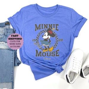 May include: A blue t-shirt featuring a Minnie Mouse graphic, paired with blue jeans and white sneakers. The graphic includes the text "MINNIE MOUSE" and the years "1928".
