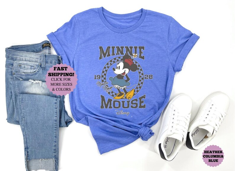 May include: A blue t-shirt featuring a Minnie Mouse graphic, paired with blue jeans and white sneakers. The graphic includes the text "MINNIE MOUSE" and the years "1928".