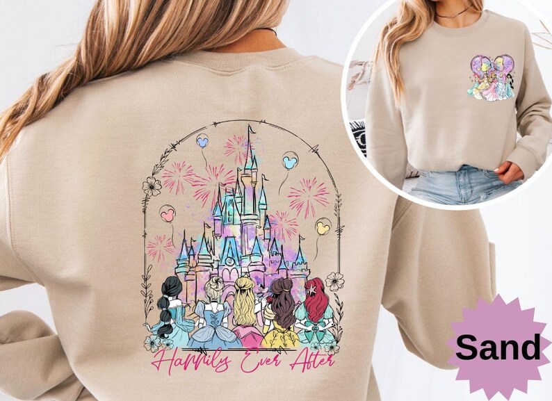 May include: Sand-colored sweatshirt featuring a colorful graphic of a fairytale castle with fireworks and balloons. The phrase "Happily Ever After" is written below the castle. A smaller graphic of princesses is on the upper right.