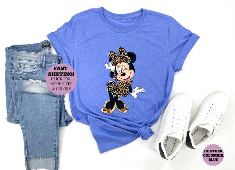 May include: A heather blue t-shirt featuring a Minnie Mouse graphic in a leopard print dress and bow. The image includes a pair of blue jeans and white sneakers. The text "Fast Shipping!" is visible.