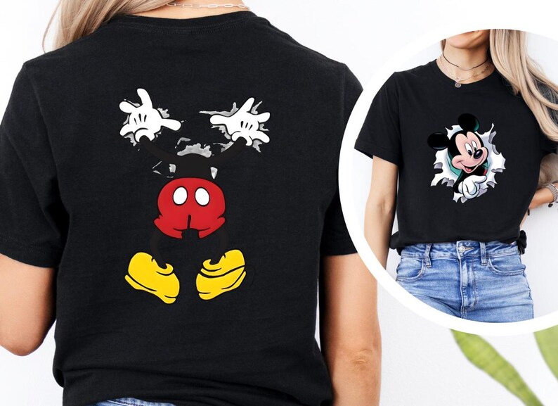 Puede incluir: Camiseta negra con un dise&ntilde;o de Mickey Mouse. La parte delantera muestra a Mickey Mouse saliendo de un agujero, y la parte trasera muestra sus manos, torso y pies. El dise&ntilde;o utiliza blanco, rojo, amarillo y negro.
