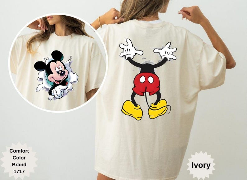 Peut inclure: T-shirt ivoire avec Mickey Mouse. L'avant pr&eacute;sente Mickey per&ccedil;ant un mur d&eacute;chir&eacute;, et le dos montre la pose embl&eacute;matique de Mickey. Le t-shirt porte le nom de la marque et le nom de la couleur.