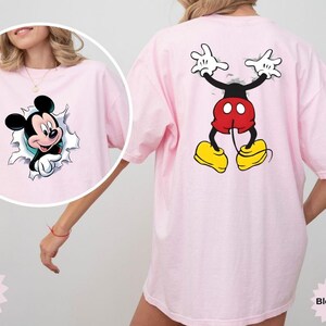 Peut inclure: T-shirt rose clair avec un motif de Mickey Mouse. L'avant du t-shirt montre Mickey per&ccedil;ant un trou d&eacute;chir&eacute;, tandis que le dos affiche le dos de Mickey. Le t-shirt est de la marque Comfort Color.