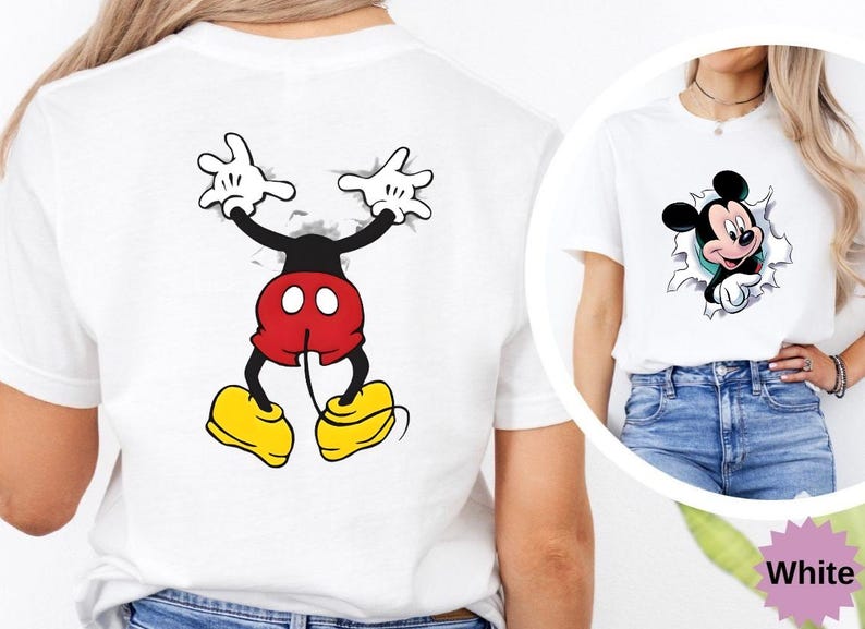 Puede incluir: Camiseta blanca con un dise&ntilde;o de Mickey Mouse. La parte delantera muestra la cara de Mickey saliendo a trav&eacute;s de un efecto rasgado, y la parte trasera muestra su cuerpo de manera similar. El dise&ntilde;o incluye los colores negro, rojo, amarillo y blanco.