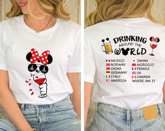 Peut inclure: T-shirt blanc avec une image de dessin animé de Minnie Mouse portant des lunettes de soleil et tenant un verre de vin. Le dos du t-shirt porte le texte "Drinking Around the World" avec une image de dessin animé des oreilles de Mickey Mouse et une chope de bière. Le texte comprend également une liste de pays avec leurs drapeaux.