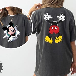 Peut inclure: T-shirt gris fonc&eacute; avec Mickey Mouse. L'avant du t-shirt montre Mickey per&ccedil;ant un trou d&eacute;chir&eacute;, tandis que le dos affiche la pose embl&eacute;matique de Mickey, les bras lev&eacute;s. Le t-shirt a un aspect vintage et d&eacute;lav&eacute;.