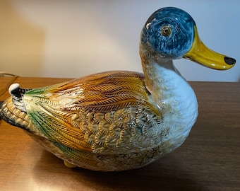 Könnte beinhalten: Eine Keramik-Entenfigur mit braunen, grünen und blauen Maldetails. Die Ente hat eine detaillierte, strukturierte Oberfläche und einen gelben Schnabel.