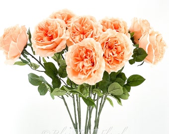 May include: A bouquet of peach-colored artificial roses in a clear glass vase. The roses have a realistic appearance and are arranged in a simple, elegant style.