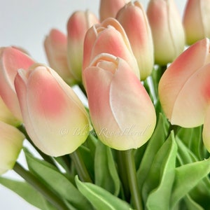 May include: A bouquet of artificial tulips with pink and white petals and green leaves. The tulips are arranged in a vase, and the stems are visible.