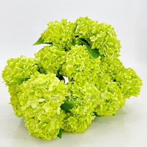 May include: A bunch of lime green artificial hydrangea flowers. The flowers are clustered together and have a realistic appearance.