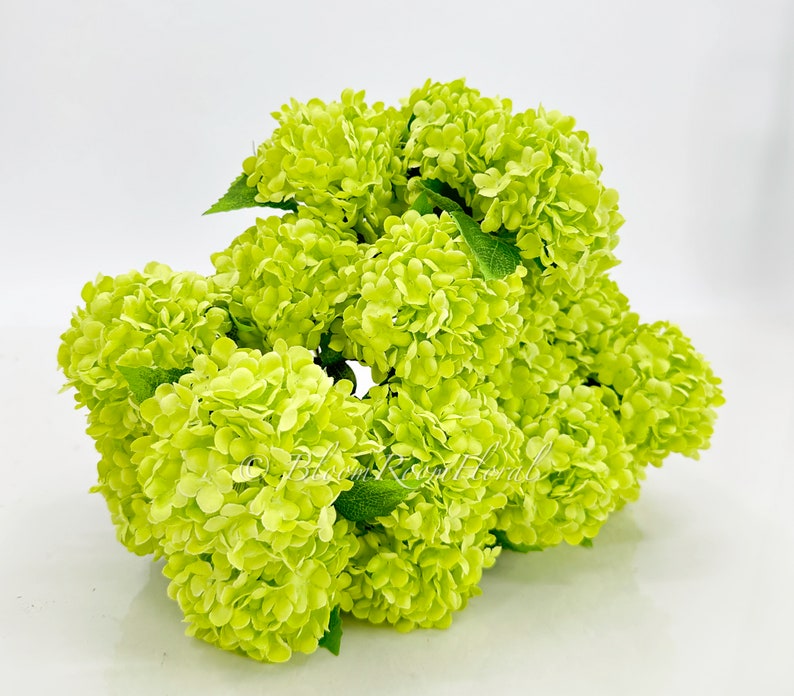 May include: A bunch of lime green artificial hydrangea flowers. The flowers are clustered together and have a realistic appearance.