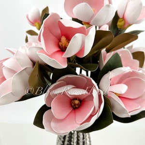 May include: A bouquet of pink and white magnolia flowers in a silver vase. The flowers are arranged in a cluster, with the stems extending out from the vase. The flowers are in full bloom, with their petals open wide. The vase is a simple, elegant design, with a silver finish.