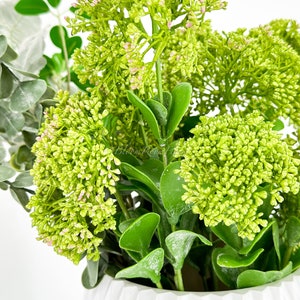 May include: A white ceramic vase with a textured surface, filled with a green and pink artificial flower arrangement.