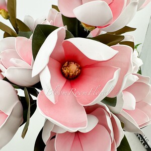 May include: A bouquet of pink and white magnolia flowers with green leaves. The flowers have a white center and pink petals.